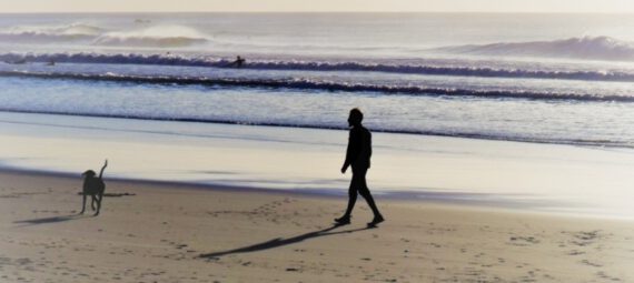 Mann mit Hund geht am Strand entlang